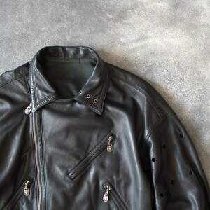 May include: Black leather jacket with an asymmetrical zip, multiple zipped pockets, and a notched collar. The jacket has a belt at the waist and decorative perforations on the sleeves.