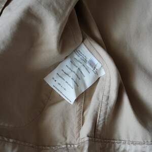 Op de afbeelding: Close-up van de binnenkant van een beige kledingstuk. Een wit label is zichtbaar, met daarop de samenstelling van het kledingstuk: 62% katoen, 38% viscose. Het label vermeldt ook "Made in Italy".