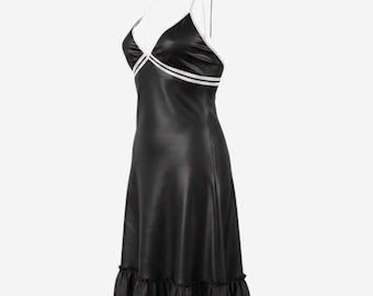 Könnte beinhalten: Ein schwarzes Slip-Kleid mit weißen Zierleisten und Spaghettiträgern. Das Kleid hat einen V-Ausschnitt, einen weißen Streifen über der Brust und einen Rüschensaum. Das Kleid ist aus glänzendem Material gefertigt.