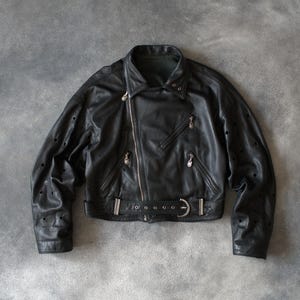 May include: Black leather biker jacket with an asymmetrical zip, notched collar, and waist belt. The jacket has decorative perforations on the sleeves and silver-toned metal hardware. A classic, stylish outerwear piece.