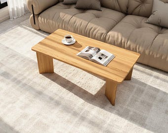 Puede incluir: Una mesa de centro rectangular de madera con acabado marrón claro. Una taza de café sobre un platillo blanco y una revista abierta descansan sobre la mesa. La mesa mide 120 cm de largo y 61 cm de ancho.