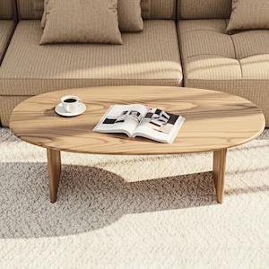 May include: Oval wooden coffee table with a light finish. A cup of coffee on a saucer and an open magazine rest on the table. The table is in front of a beige sectional sofa and sits on a white rug.