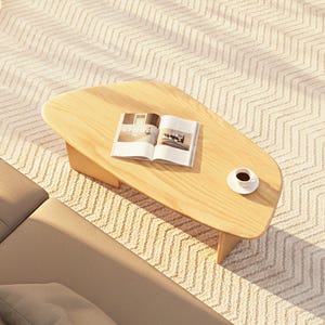 May include: A light wood coffee table with an organic shape, a magazine, and a cup of coffee on a saucer. The table is on a patterned rug, next to a beige sofa.
