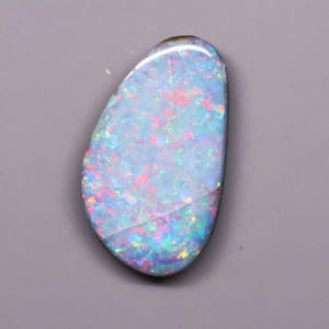 May include: A polished, teardrop-shaped opal gemstone featuring a vibrant play-of-color with dominant flashes of bright blue, light cyan, and scattered specks of pink and orange throughout its smooth, reflective surface against a neutral background.