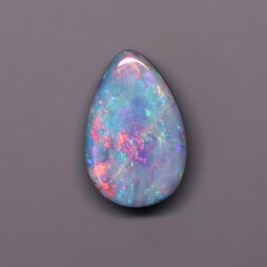May include: A pear-shaped opal gemstone featuring a translucent body with a vibrant play-of-color. The stone displays flashes of bright red, electric blue, and green hues scattered across its surface, creating a dynamic and iridescent appearance.