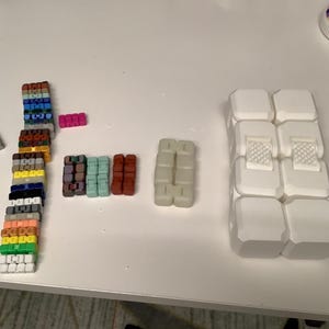 Puede incluir: Un surtido de bloques de construcción geométricos coloridos en varios tamaños y colores, incluyendo blanco, verde, amarillo, azul y rosa. Algunos bloques están apilados, mientras que otros están dispuestos por separado sobre una superficie blanca.