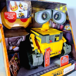 May include: A yellow and gray WALL-E toy robot in its original box. The toy has large, binocular-like eyes and articulated arms. The box includes text in multiple languages, including "Remote-controlled" and "20+ Lights & Sounds."