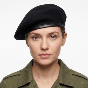 May include: A solid black beret featuring a smooth, rounded crown and a distinct black leather trim band encircling the base. The hat is constructed from a soft, felt-like material and sits firmly on the head, maintaining a structured shape.
