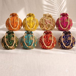 May include: Eight round drawstring pouches in orange, yellow, cream, magenta, green, teal, red, and navy blue. Each pouch features intricate gold floral embroidery and a beaded handle made of small white pearls, creating a uniform collection.