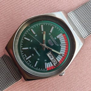 Peut inclure: Une montre automatique Seiko vintage avec un cadran vert et un boîtier argenté. La montre est dotée d'un bracelet en maille et d'un affichage de la date. Le cadran comporte des index et des aiguilles blancs. Le cadran de la montre présente des accents rouges et blancs.
