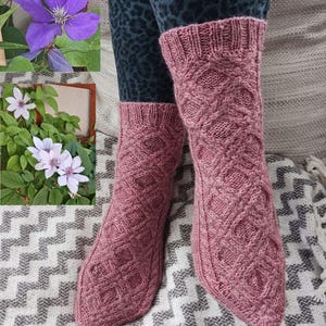 May include: A pair of rose-colored knitted socks with a diamond pattern. The socks are worn over patterned leggings and rest on a patterned blanket. The socks have a ribbed cuff and a textured design.