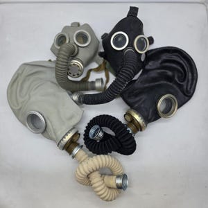 Può includere: Una collezione di quattro maschere antigas dotate di tubi flessibili corrugati e oculari circolari in vetro con bordi metallici. Le maschere sono nei toni del grigio e del nero, con due maschere collegate a lunghi tubi avvolti in beige e nero.