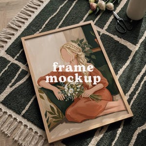 May include: A framed art print mockup with a woman holding flowers, with the text "frame mockup". The frame is light brown, and the artwork is set on a green and white patterned rug. The image also includes a book and scissors.