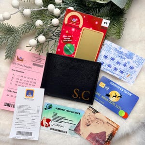May include: A black leather wallet with the gold initials S.C. surrounded by a North Pole lottery ticket, a Kringles Bank card, a Sleigh Flying Licence, a Frosty Coffee loyalty card, a receipt, a scratch card, and a photo of Santa and Mrs. Claus.
