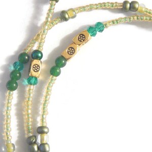 K&ouml;nnte beinhalten: Eine gr&uuml;ne und goldene Perlenkette mit einem goldenen Verschluss. Die Kette besteht aus kleinen, runden Perlen und hat ein paar gr&ouml;&szlig;ere, quadratische Perlen.