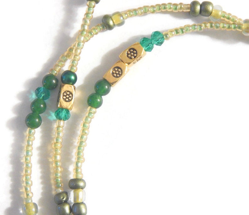K&ouml;nnte beinhalten: Eine gr&uuml;ne und goldene Perlenkette mit einem goldenen Verschluss. Die Kette besteht aus kleinen, runden Perlen und hat ein paar gr&ouml;&szlig;ere, quadratische Perlen.