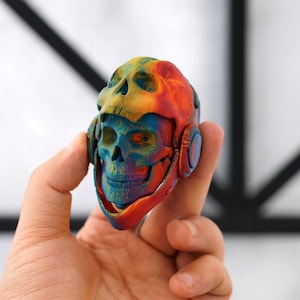 Op de afbeelding: Een veelkleurig, 3D-geprint schedelbeeldje, vastgehouden in een hand. De schedel heeft een kleurengradiënt met rood, oranje, geel, blauw en groen. Het ontwerp omvat oogkassen, een neusholte en een kaak.