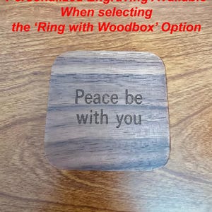 K&ouml;nnte beinhalten: Eine quadratische Holzbox mit abgerundeten Ecken, graviert mit den Worten "Peace be with you". Die Box hat eine nat&uuml;rliche Holzmaserung. Der Text oben lautet "Personalisierte Gravur verf&uuml;gbar bei Auswahl der Option 'Ring with Woodbox'."