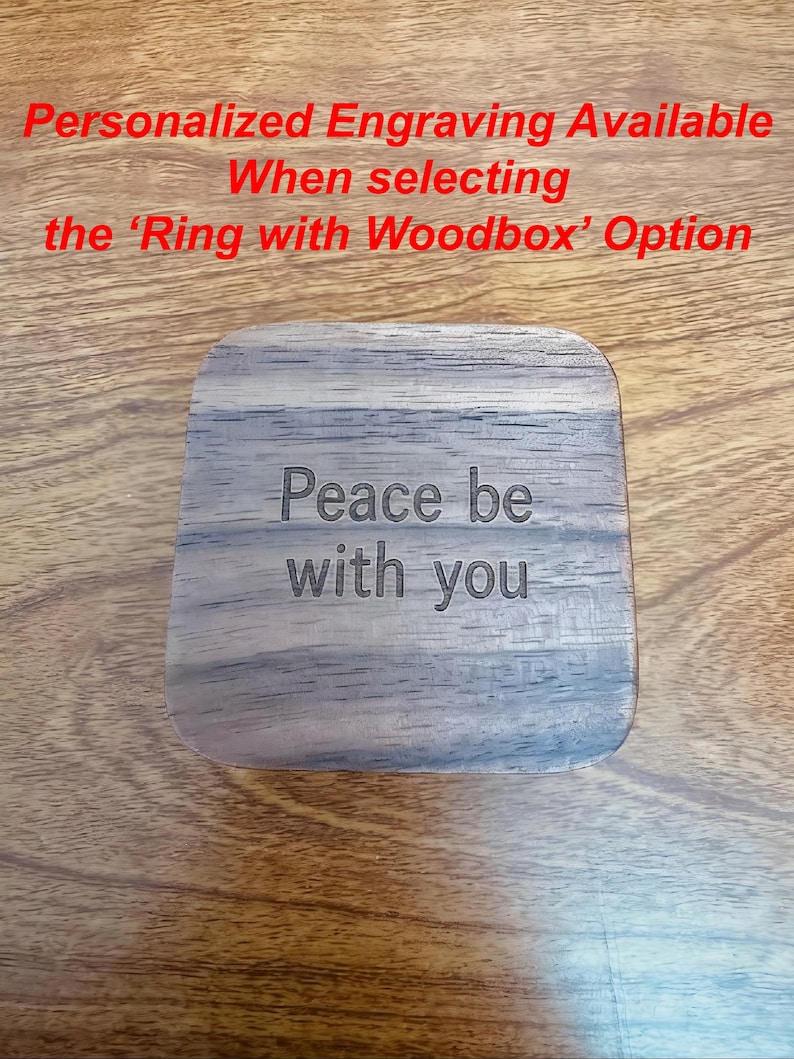 K&ouml;nnte beinhalten: Eine quadratische Holzbox mit abgerundeten Ecken, graviert mit den Worten "Peace be with you". Die Box hat eine nat&uuml;rliche Holzmaserung. Der Text oben lautet "Personalisierte Gravur verf&uuml;gbar bei Auswahl der Option 'Ring with Woodbox'."