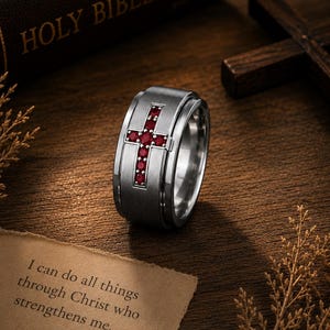 May include: A brushed silver-tone metal ring featuring a central cross inlay set with small red stones. The ring is displayed alongside a Bible and a piece of paper with the text: I can do all things through Christ who strengthens me. Philippians 4:13.