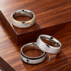 以下が含まれることがあります： 十字架のデザインが施された3つのステンレススチールリング。1つのリングは「EARTH」の文字と十字架が入ったゴールドバンド。別のリングは十字架の入ったブラックバンド。3つ目のリングには刻まれたテキストと十字架があります。