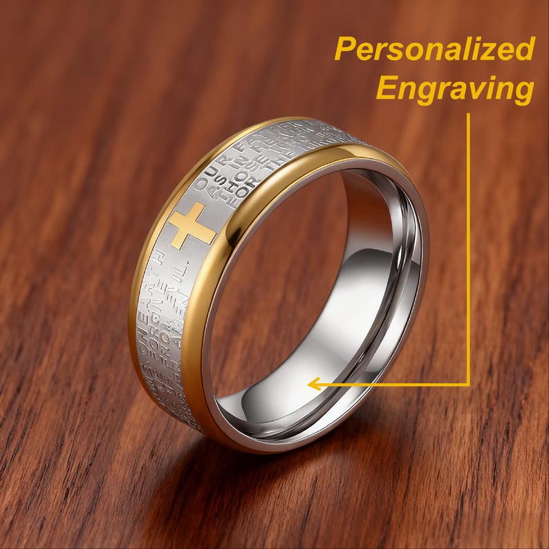 K&ouml;nnte beinhalten: Ein gold- und silberfarbener Ring mit Kreuz und eingraviertem Text. Der Ring hat ein goldenes Band und ein silbernes Innenteil. Der Text "Personalized Engraving" ist im Bild zu sehen.