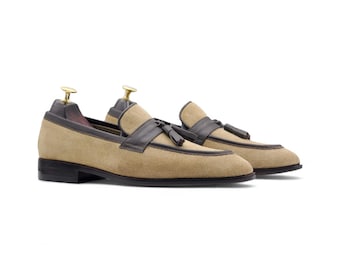 May include: A pair of tan suede loafers with dark brown leather accents and small tassels. The shoes have a classic design with a low heel and a sleek silhouette, perfect for a formal or casual look.