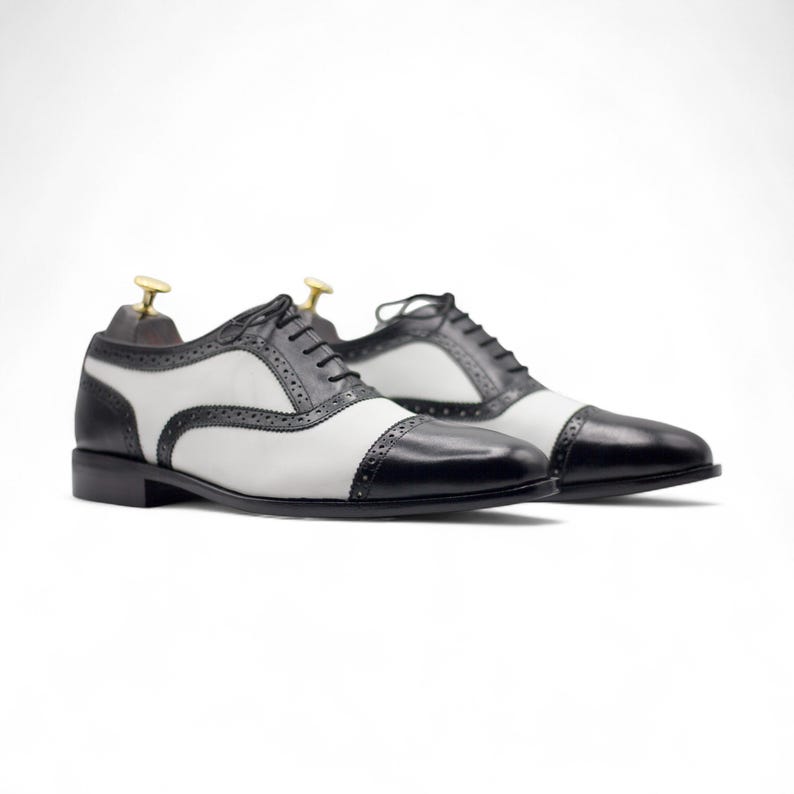 Side profile showing the classic cap toe design and sleek black and white leather finish, suitable for weddings and events.