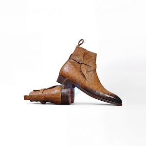 May include: A pair of brown leather ankle boots with a textured pattern. The boots have a pointed toe, a strap with a buckle, and a pull tab at the back. The boots are approximately 15 cm tall.
