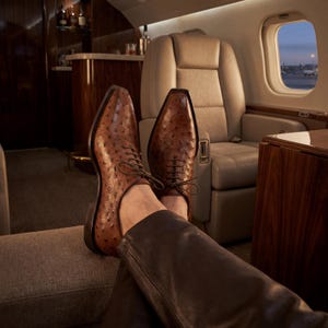 Angled top down view of pair of men handmade cognac full quill ostrich wholecut Oxford shoes with cedar shoe trees showing quill texture across full surface on grey background