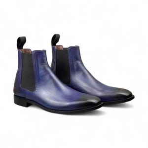 Peut inclure: Paire de bottines Chelsea bleues avec un effet dégradé, passant du bleu foncé au noir au bout. Les bottines ont des empiècements latéraux élastiques noirs et des tirettes. Le cuir semble lisse et poli.