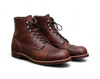 Puede incluir: Un par de botas de cuero marrón con diseño de puntera. Las botas tienen cierre de cordones con ojales metálicos y suela resistente. El cuero tiene un aspecto envejecido, y las botas están sobre un fondo blanco.