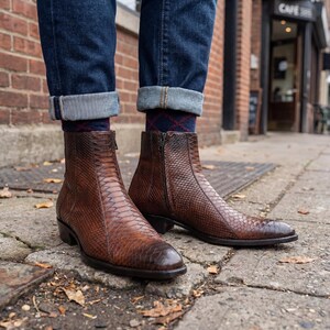 Close-up of men's brown snakeskin zip boots styled with cuffed blue denim jeans.