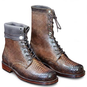 May include: A pair of brown leather lace-up boots with a snakeskin pattern. The boots have a high-top design with multiple eyelets for the laces and a contrasting gray collar. The soles are a darker brown.