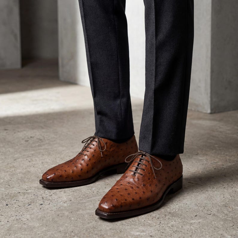 Front facing top down view of pair of men cognac ostrich leather wholecut Oxford shoes with cedar shoe trees showing closed lacing throat and square toe on white background