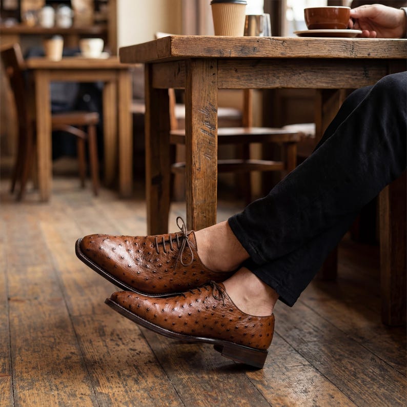 Pair of men handmade cognac full quill ostrich wholecut Oxford shoes with cedar shoe trees placed on urban street curb at night with neon city lights bokeh in background