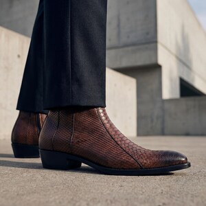 High-fashion shot of polished brown python leather boots and black dress pants.