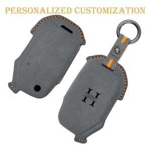 May include: Two gray key fob cases with the text "PERSONALIZED CUSTOMIZATION" at the top. One case is open, and the other is closed. The open case has a silver keyring attached with an orange accent. The closed case has the initials "II" and the name "HENRY" printed on it.