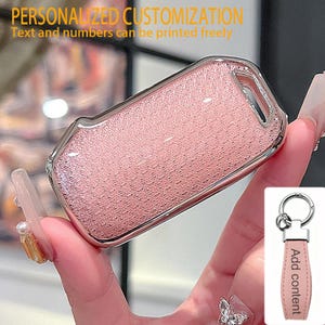 May include: A rectangular pink car key fob cover with a textured surface and a metallic silver border. The text PERSONALIZED CUSTOMIZATION Text and numbers can be printed freely appears at the top. Includes a pink keychain with the text Add content.