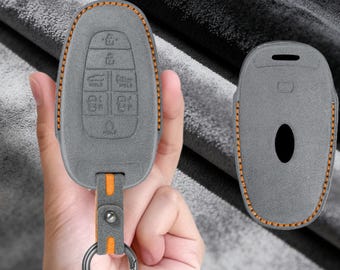 May include: A grey key fob cover with orange stitching and an orange strap featuring a metal ring. The cover displays embossed icons for lock, unlock, trunk, and hold functions. The text PERSONALIZED CUSTOMIZATION is visible at the top.