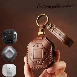 May include: A brown leather key fob case with a gold-coloured clasp and a matching leather tag. The tag is engraved with the name "David" and the date "1995.06.01". The case has a stitched border and embossed key symbols. The text "Customizable content" is at the top.