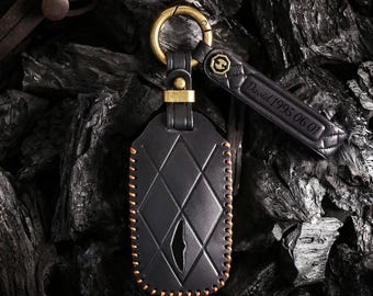 May include: Black leather key fob with a diamond pattern and orange stitching. The fob has a gold-colored clasp and a matching leather tag with the engraved text "David 1995.06.01". The key fob is designed to hold a car key.