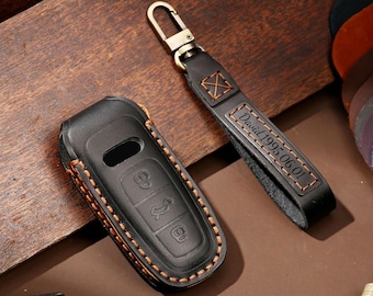 Könnte beinhalten: Schwarze Leder-Schlüsselanhänger-Hülle und passender Schlüsselanhänger mit goldfarbener Hardware. Die Schlüsselanhänger-Hülle hat orangefarbene Nähte und geprägte Schlüsselsymbole. Der Schlüsselanhänger ist mit "David 1995 06 01" graviert.