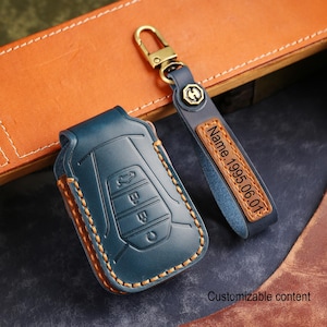May include: A teal leather car key fob cover and matching keychain with gold-colored hardware. The key fob cover has an embossed car design and orange stitching. The keychain has a leather tag with the text "Name. 1995.06.01". The text "Customizable content" is also visible.