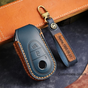 Puede incluir: Una funda para llave de coche de cuero azul con ribete de cuero marrón y costuras naranjas. Un llavero de cuero azul a juego con un cierre dorado y una etiqueta de cuero marrón con el texto "Name 1995.06.01". También se ve el texto "Customizable content".