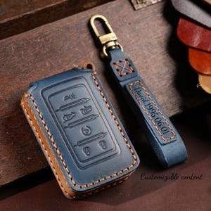 Peut inclure: Étui de clé de voiture en cuir bleu et porte-clés assorti. L'étui de la clé comporte des boutons en relief et est cousu avec du fil beige. Le porte-clés porte l'inscription "David 1995.06.01" et un fermoir en métal. Le texte "Customizable content" est également visible.