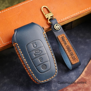 Puede incluir: Una funda azul de cuero para la llave del coche con costuras naranjas y un llavero a juego. El llavero tiene una etiqueta de cuero con el texto "Name.1995.06.01". El llavero tiene botones para bloquear, desbloquear y el maletero.