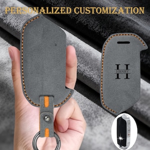 May include: Gray leather key fob cover with orange stitching and accents. The cover has a key ring and a snap closure. The text "PERSONALIZED CUSTOMIZATION" is at the top. The cover is personalized with the initials "II HRNRY II".