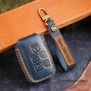 May include: A blue leather car key fob cover and a matching keychain. The key fob cover has embossed buttons and a contrasting brown stitched border. The keychain has a gold-coloured clasp and a leather tag with the text "Name. 1995.06.01".