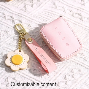 Pode incluir: Uma capa de chave de carro em couro rosa claro, uma alça de chaveiro combinando com o texto "customized text" e um chaveiro em forma de margarida com corrente e ferragens douradas. O texto "Customizable content" está na parte inferior.